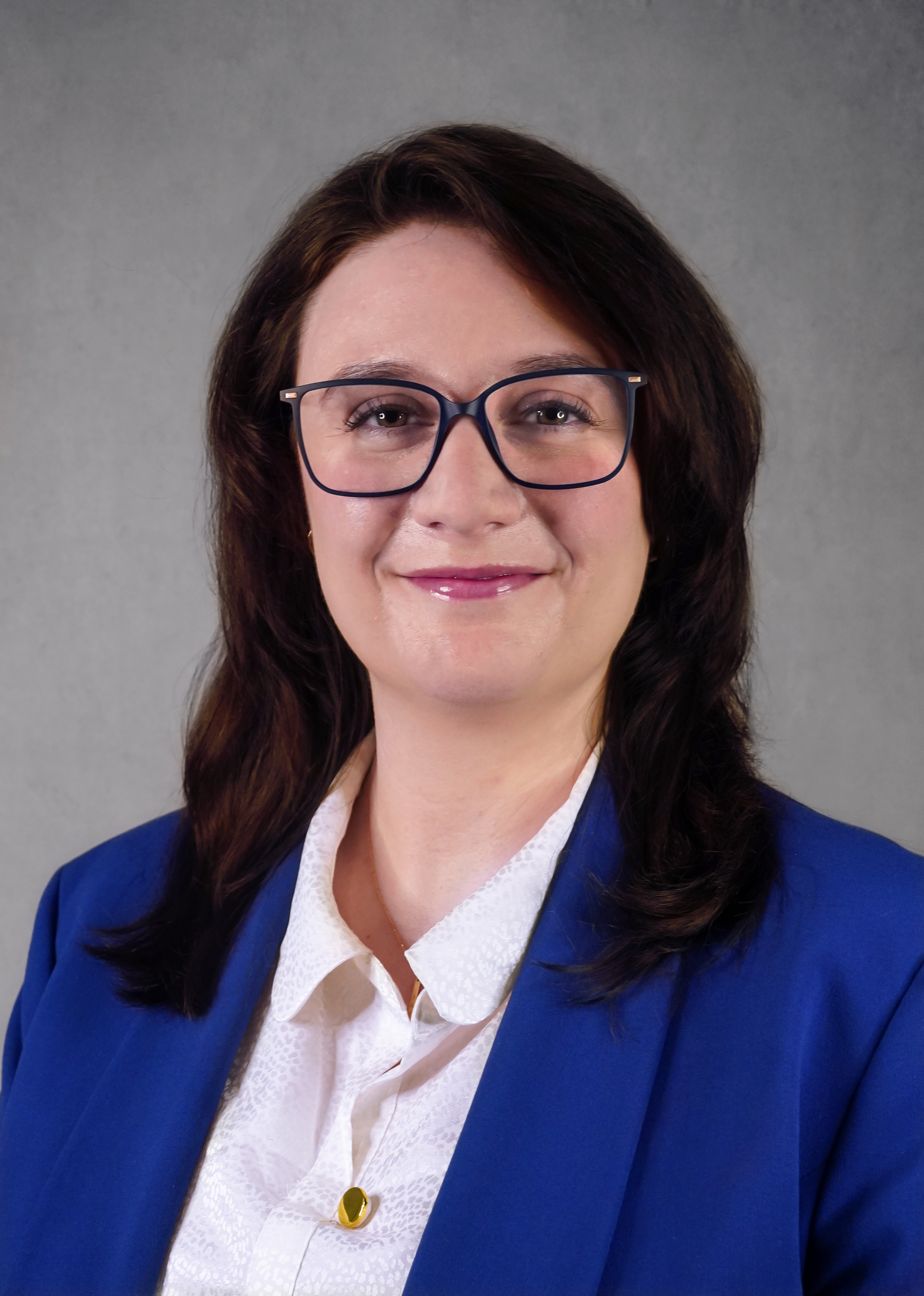 A person with brown hair that is wearing a white shirt under a pink blazer.